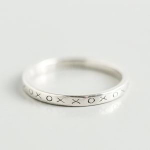 May include: A silver band ring with the inscription "XOXO" around the entire band.