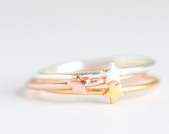 May include: Three delicate stacking rings with star accents. The rings are silver, rose gold, and gold.