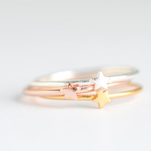 May include: Three delicate stacking rings with star accents. The rings are silver, rose gold, and gold.