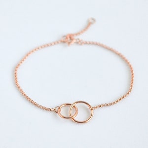 May include: A delicate rose gold bracelet featuring two interlocking circles. The bracelet is made from a fine chain and has a simple, elegant design.