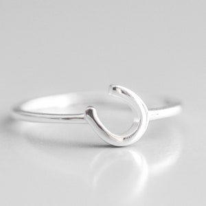 Puede incluir: Un anillo de plata con un dise&ntilde;o simple de 'C' curvado.