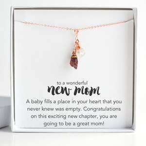 Puede incluir: Una caja de regalo blanca con un collar de oro rosa dentro. El collar tiene un colgante de cristal rojo y blanco. La caja tiene un mensaje que dice: "a una maravillosa nueva mam&aacute;. Un beb&eacute; llena un lugar en tu coraz&oacute;n que nunca supiste que estaba vac&iacute;o. Felicitaciones por este emocionante nuevo cap&iacute;tulo, &iexcl;vas a ser una gran mam&aacute;!"