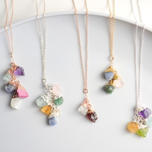 Pode incluir: Cinco colares delicados com pingentes de pedras preciosas brutas. Cada colar apresenta uma combinação diferente de pedras preciosas coloridas, incluindo ametista, água-marinha, quartzo rosa, esmeralda, safira, citrino, granada e topázio.