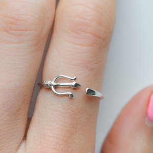May include: A silver ring with a trident design. The ring is open and adjustable.