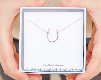Puede incluir: Un collar de herradura de oro rosa en una caja blanca con el sitio web "www.silverandivy.com" impreso en la parte inferior.