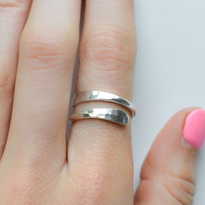 May include: A silver hammered wrap ring with a simple design. The ring is worn on a finger with pink nail polish.