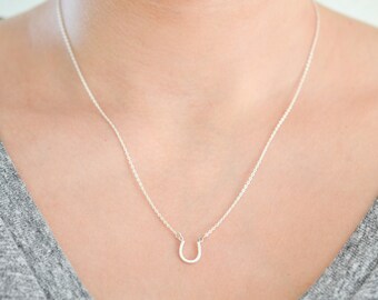 Puede incluir: Un collar de cadena de plata con un pequeño colgante de herradura.