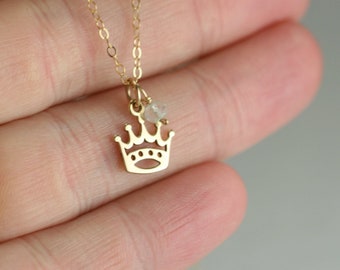 May include: A gold chain necklace with a delicate crown pendant and a small clear gemstone charm.