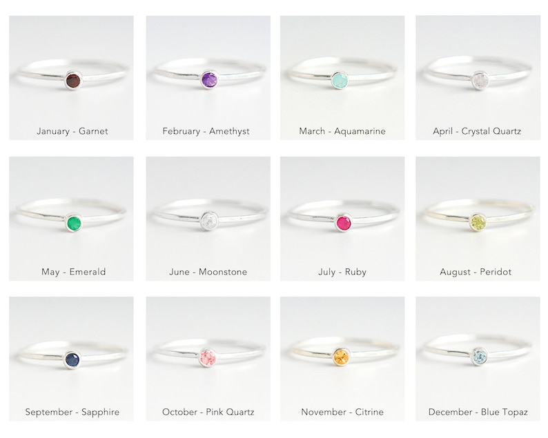 May include: Twelve silver rings with a small gemstone in the center. Each ring represents a different month of the year and features a corresponding birthstone. The birthstones are: Garnet, Amethyst, Aquamarine, Crystal Quartz, Emerald, Moonstone, Ruby, Peridot, Sapphire, Pink Quartz, Citrine, and Blue Topaz.