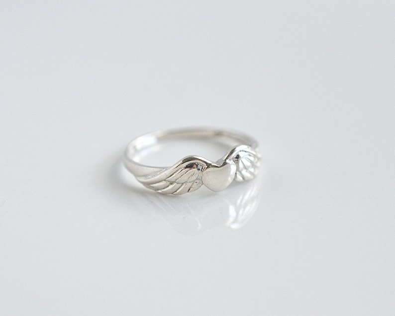 May include: A silver ring with a heart-shaped design and wings on either side.