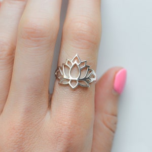 Puede incluir: Un anillo de plata con un diseño de flor de loto. El anillo está en un dedo.