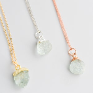 May include: Three delicate necklaces with raw aquamarine crystal pendants. The necklaces are available in gold, silver, and rose gold.