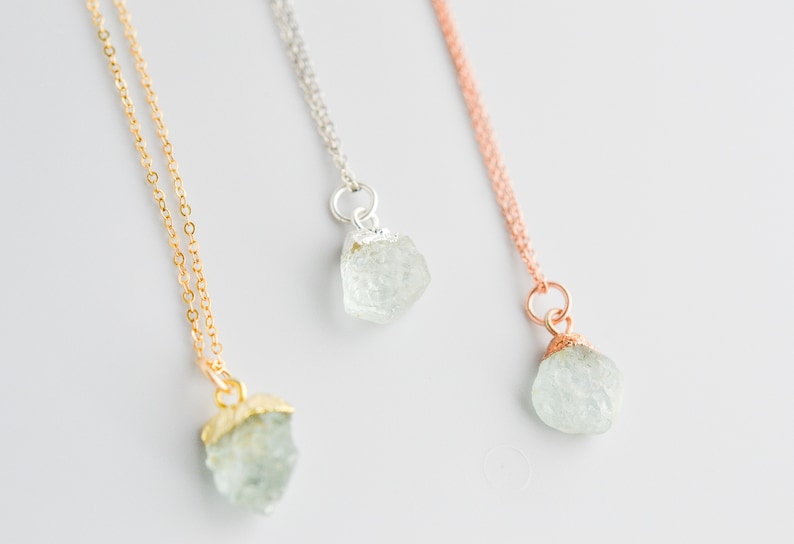 May include: Three delicate necklaces with raw aquamarine crystal pendants. The necklaces are available in gold, silver, and rose gold.