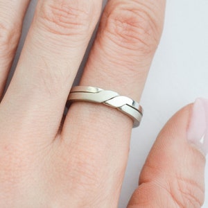 Peut inclure: Une alliance en argent avec un design tressé unique. La bague est portée à l'annulaire d'une main.