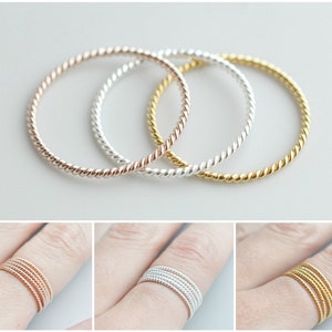 May include: Three thin, twisted metal rings in silver, gold, and rose gold. The rings are stacked on top of each other.