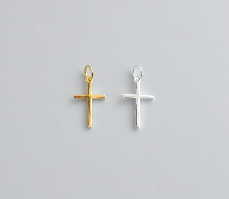 Sterling silver and gold cross charms lying flat on a white background, highlighting the smooth surface and precise 16x9.5mm shape.