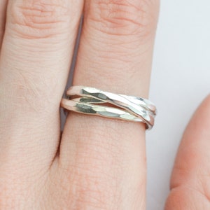 Könnte beinhalten: Ein silberner Ring mit gehämmerter Oberfläche. Der Ring besteht aus drei miteinander verschlungenen Bändern.