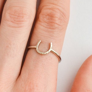 May include: A silver horseshoe ring on a finger.