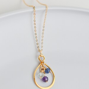 May include: A gold chain necklace with a teardrop-shaped pendant. The pendant has three small gemstones: a light blue aquamarine, a dark blue sapphire, and a purple amethyst.