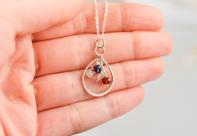 May include: A silver necklace with a teardrop-shaped pendant. The pendant is filled with small pink, red, and blue gemstones.