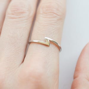 Könnte beinhalten: Ein silberner Ring mit minimalistischem Zickzack-Design. Der Ring ist dünn und filigran und wird an einem Finger getragen. Der Hintergrund ist eine verschwommene, neutrale Farbe.
