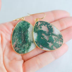 May include: A pair of gold dangle earrings with green and pink agate stone drops. The stones have a unique, marbled pattern.