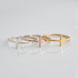 May include: Three simple cross rings in silver, rose gold, and gold.