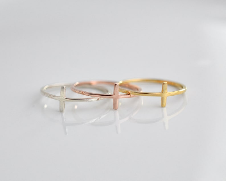 May include: Three simple cross rings in silver, rose gold, and gold.