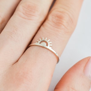 May include: A silver ring with a sun design. The sun is a simple outline with rays.