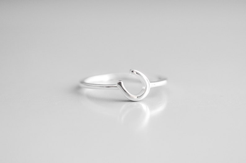 Puede incluir: Un anillo de plata con un dise&ntilde;o simple de 'C' curvado.