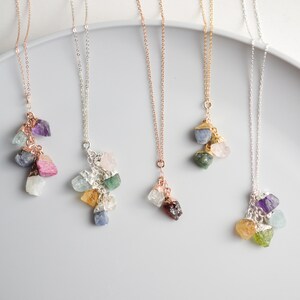 Puede incluir: Cinco delicados collares con dijes de piedras preciosas en bruto. Cada collar presenta un racimo de piedras preciosas de diferentes colores, incluyendo amatista, aguamarina, cuarzo rosa, aventurina verde y citrino.