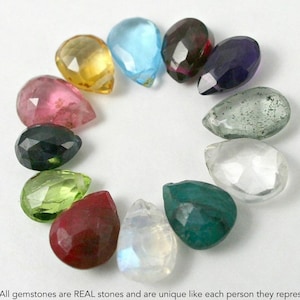 May include: A collection of 12 teardrop-shaped gemstones in various colors, including blue, green, red, pink, and clear. The gemstones are arranged in a circle on a white background.