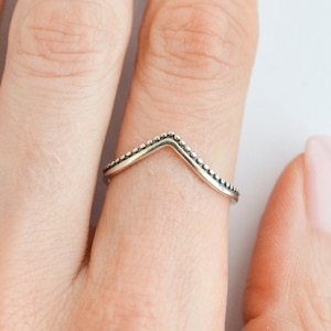 Może przedstawiać: Srebrny pierścionek z wzorem w kształcie litery V i ozdobnym brzegiem z perełek.