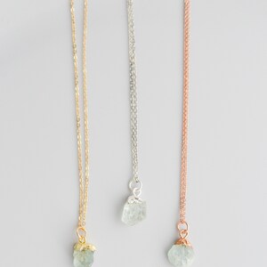 May include: Three delicate necklaces with raw aquamarine crystal pendants. The necklaces are available in gold, silver, and rose gold chain styles.
