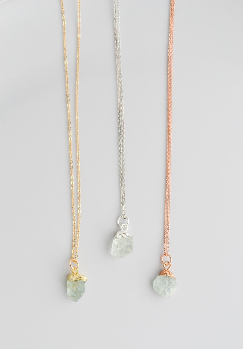 May include: Three delicate necklaces with raw aquamarine crystal pendants. The necklaces are available in gold, silver, and rose gold chain styles.