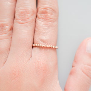 K&ouml;nnte beinhalten: Ein zarter Goldring mit Perlenmuster. Der Ring wird an einem Finger getragen.