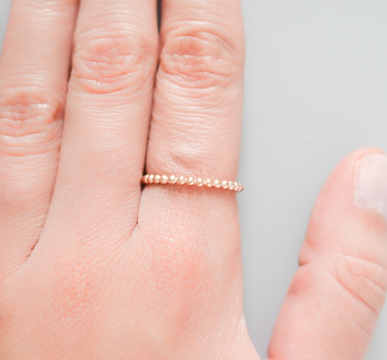 K&ouml;nnte beinhalten: Ein zarter Goldring mit Perlenmuster. Der Ring wird an einem Finger getragen.