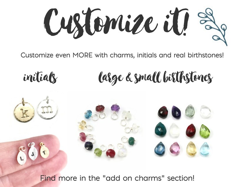 May include: A close-up of a variety of charms for jewelry making. The charms include small initial letters, birthstones, and small charms. The text "Customize it!" is at the top of the image. The text "Customize even MORE with charms, initials and real birthstones!" is below the first text. The text "initials" is above a row of two charms with the letters "K" and "M". The text "large & small birthstones" is above a row of birthstones. The text "Find more in the "add on charms" section!" is at the bottom of the image.