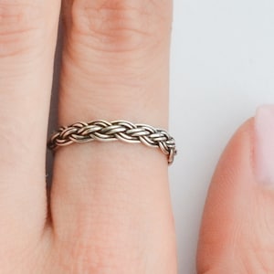 May include: A silver braided ring worn on a finger.