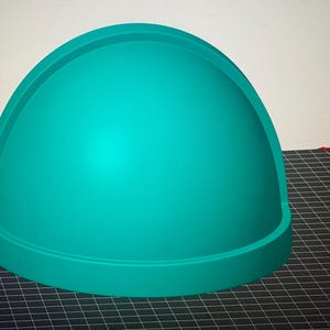 May include: A solid teal dome-shaped object with a smooth, matte finish. The structure features a curved top section that transitions into a flat, circular base rim, creating a distinct semi-spherical form with a uniform, vibrant color throughout.