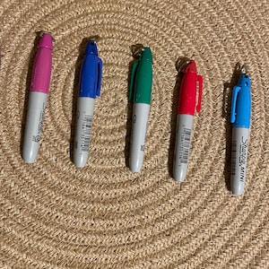May include: A set of ten colorful Sharpie mini markers with silver caps. The markers are arranged in a row on a woven surface. The colors are purple, pink, blue, green, red, blue, black.