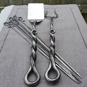 May include: A set of twisted metal grilling tools, including a spatula, a fork, and six skewers. The tools have a rustic, hand-forged look.
