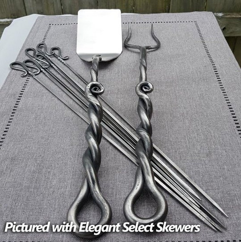May include: A set of twisted metal fireplace tools, including a poker, a shovel, and six skewers. The tools have a rustic, hand-forged look and are pictured on a gray fabric background.