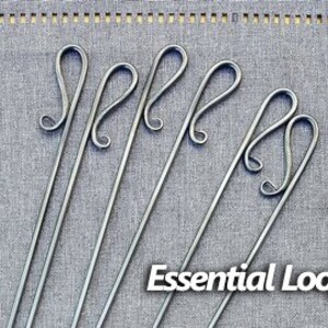 May include: Six silver metal skewers with a decorative loop at the top. The skewers are arranged in a row on a gray fabric background. The text "Essential Loop" is printed below the skewers.