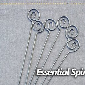 May include: Set of six silver metal skewers with a spiral design and a small loop at the top. The skewers are arranged in a row on a gray fabric background. Essential Spiral is written in black text below the skewers.