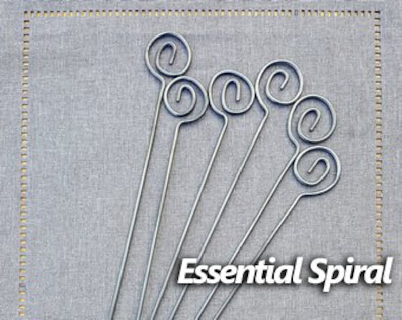 May include: Set of six silver metal skewers with a spiral design and a small loop at the top. The skewers are arranged in a row on a gray fabric background. Essential Spiral is written in black text below the skewers.