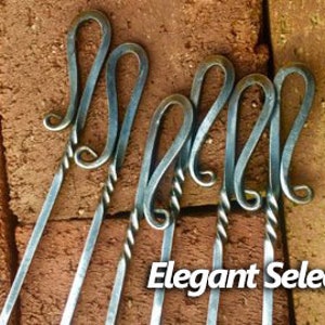May include: Set of four silver metal skewers with twisted handles and decorative loops at the top. The skewers are arranged on a brick background. The text "Elegant Select" is visible at the bottom of the image.