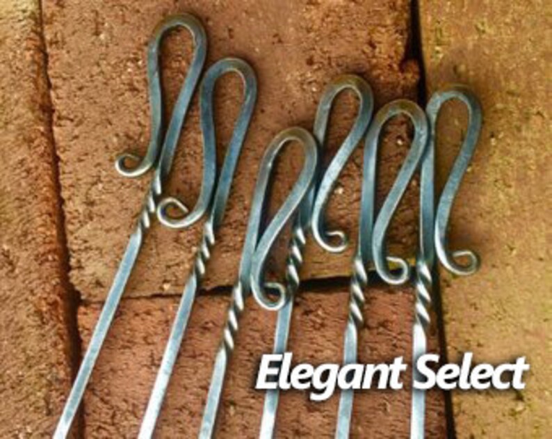 May include: Set of four silver metal skewers with twisted handles and decorative loops at the top. The skewers are arranged on a brick background. The text "Elegant Select" is visible at the bottom of the image.