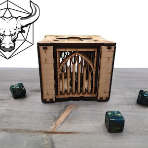 May include: A wooden dice tower with a gothic arch design, surrounded by three green and blue dice. A black and white bull head logo is in the upper left corner. The tower is made of light brown wood.