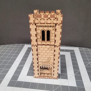May include: A wooden model of a medieval tower, featuring a detailed brickwork design. The tower has arched windows and a gated entrance. The natural wood color highlights the intricate laser-cut details, perfect for tabletop gaming or display.